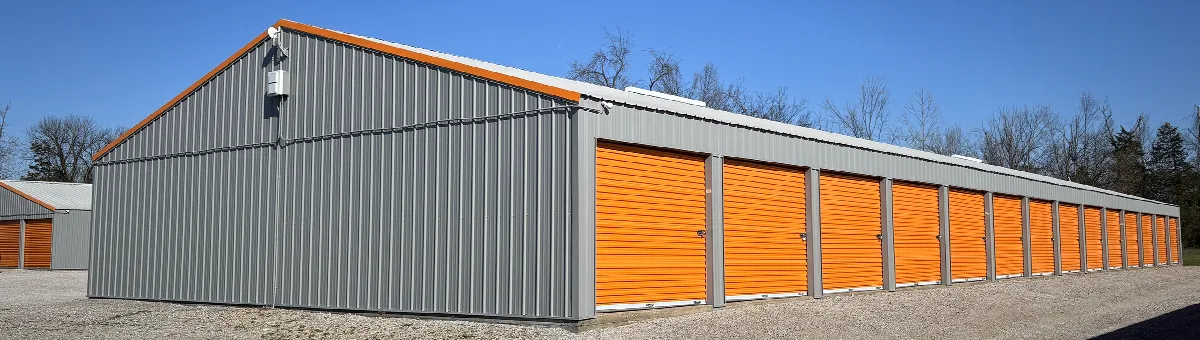 Gray metal self-storage building with orange roll-up doors and orange roof trim.