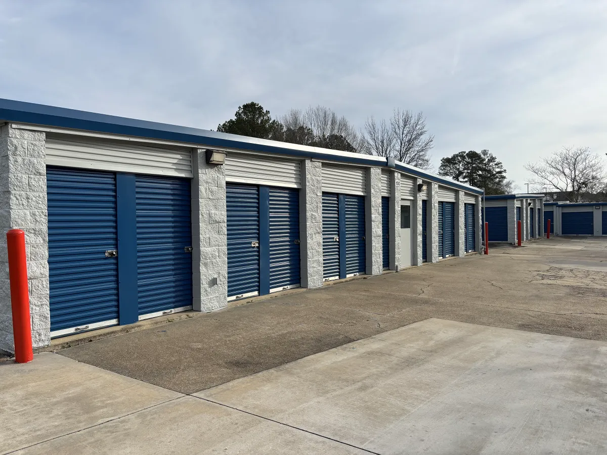 White concrete self-storage buildings with blue roll-up doors and red bollards.